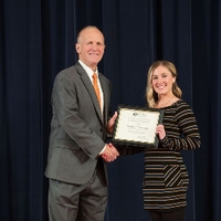 Doctor Potteiger posing for a photo with an award recipient in a black, grey, and white striped sweater dress